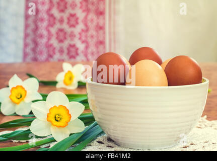 On the table on a lace napkin stands a vase with Easter eggs. Next to it lay a large white daffodils. Stock Photo
