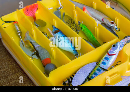 In a plastic yellow container with a large number of cells are a variety of shiny lures to catch fish. Stock Photo
