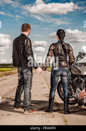 Biker man and girl stands on the road and looks into the distance Stock Photo