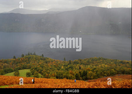 View over Derwentwater from Catbells, with rain squall over the lake and walkers decsending through bracken covered fellside, Cu Stock Photo