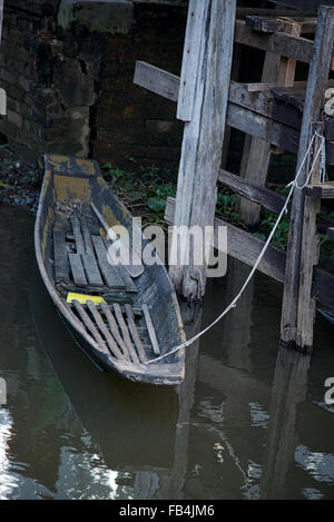 A dilapidated wooden boat rests on the end of a tattered rope along the pilings of a pier on Inle Lake in Myanmar. Stock Photo