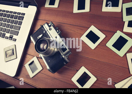composition of old fashioned photo camera, laptop and photo slides on wooden table Stock Photo