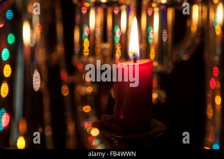 Red candle close-up with colorful light bokeh in the background. Stock Photo