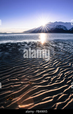 Sunset at low tide with patterns in the sand on a Southeast Alaskan beach with a snow covered mountain in the background. Stock Photo