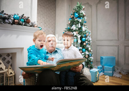 Senior man reading a book to grandsons at Christmas Eve Stock Photo