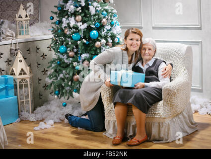Senior woman and her adult granddaughter holding a gift against a Christmas tree Stock Photo