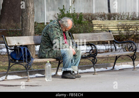 A homeless man is sitting and sleeping on a bench in a park in Bulgaria's capital Sofia. Years after joining the EU the country  Stock Photo