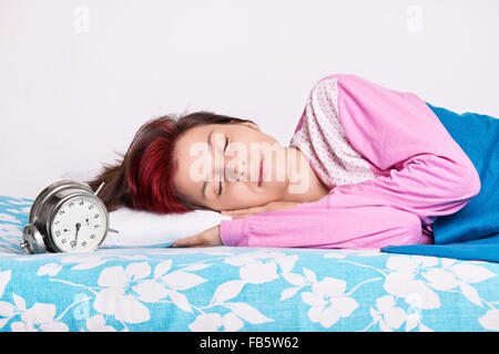 Beautiful young girl in pink pajamas calmly sleeping in her bed next to an old fashioned alarm clock. Healthy sleeping concept. Stock Photo