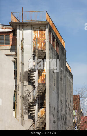 Rusting fire escape on a derelict building. Rust and flaking paint on an old apartment block set against a blue sky in Penang. Stock Photo