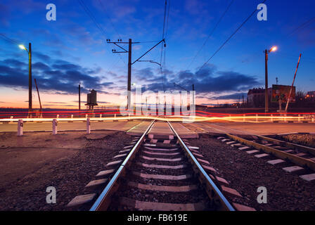 Railroad crossing with car lights in motion at night. Stock Photo