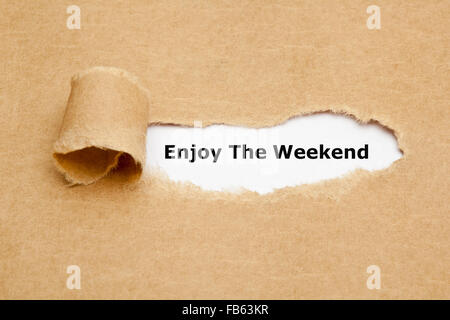 The text Enjoy The Weekend appearing behind torn brown paper. Stock Photo