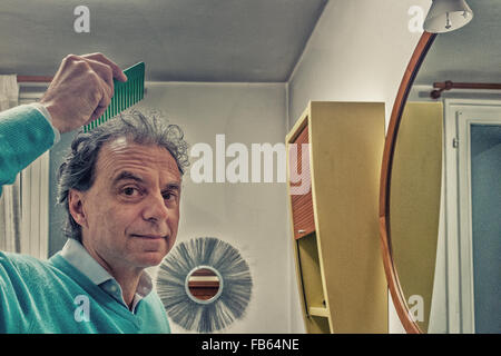 balding fifty man combing his hair in the bathroom before the mirror Stock Photo