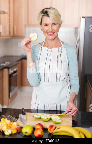 pretty middle aged woman tasting apple while preparing salad Stock Photo