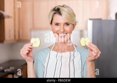 happy senior woman holding slices of apple in kitchen Stock Photo