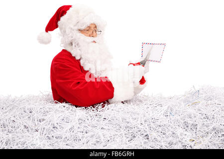 Studio shot of Santa Claus cutting a letter with scissors and standing in a pile of shredded paper isolated on white background Stock Photo