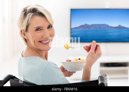 happy handicapped elderly woman eating fruit salad at home Stock Photo