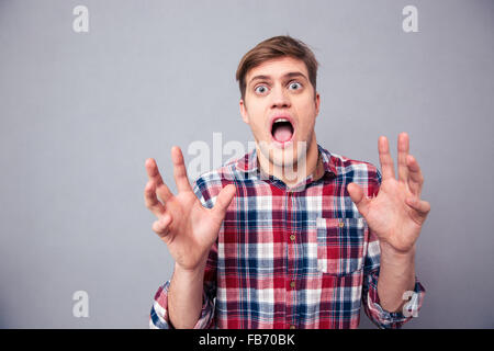 Portrait of terrified frightened young man in checkered shirt screaming with open mouth over grey background Stock Photo