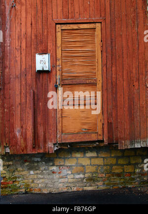Metallic mailbox on the red wood wall next to aged cracked red wood door above the brick wall Stock Photo