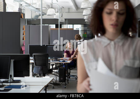 Colleagues discussing in office, Woman with documents in foreground Stock Photo