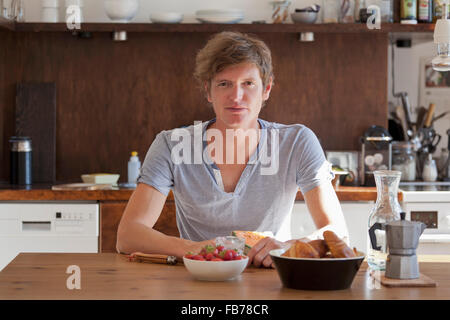 Young man sitting at dining table with breakfast, portrait Stock Photo