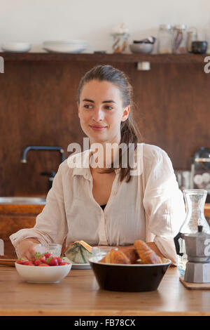 Young woman sitting at dining table with breakfast, smiling Stock Photo