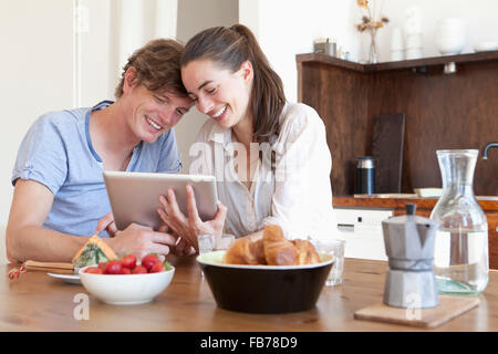 Young couple sitting at dining table, using digital tablet Stock Photo