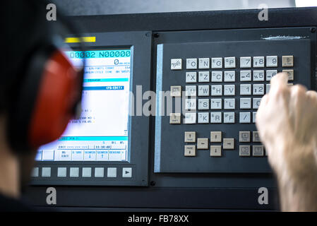 CNC operator, mechanical technician worker at metal machining milling center in tool workshop inserting data with keyboard weari Stock Photo