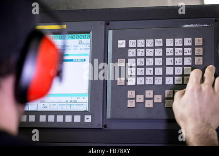 CNC operator, mechanical technician worker at metal machining milling center in tool workshop inserting data with keyboard weari Stock Photo