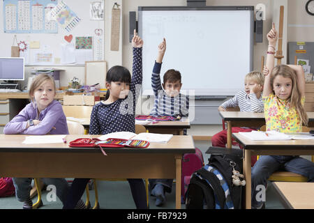 Students raising their hands in classroom Stock Photo