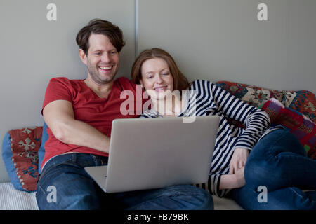 Couple using laptop while lying on sofa Stock Photo