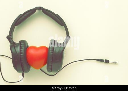 soft toned image of black headphones with red heart, wires and socket on yellow background Stock Photo