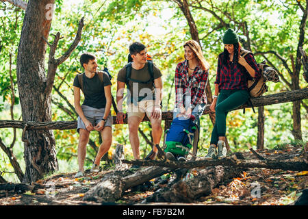 Full length of friends sitting on wooden log in forest Stock Photo