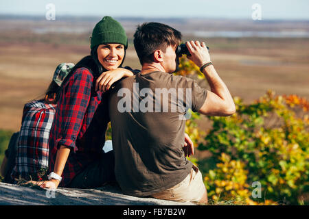 Happy young woman sitting with friend using Binoculars in forest Stock Photo
