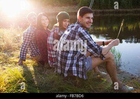 Portrait of friends sitting with man at lakeshore Stock Photo