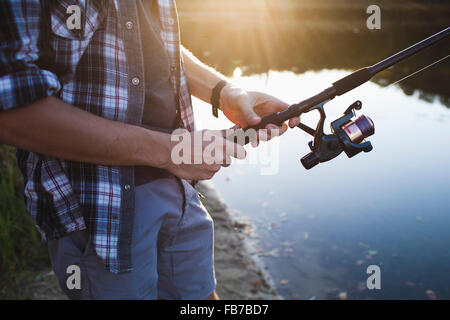 Midsection of man fishing at lakeshore in forest Stock Photo