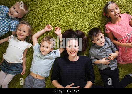 Directly above shot of happy female teacher and students lying on rug in classroom Stock Photo