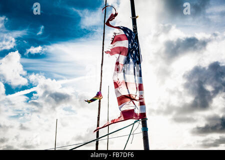 Tattered American flag on pole against cloudy sky Stock Photo