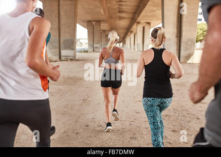 Rear view of group of athletes running under a bridge. Runners training together. Stock Photo