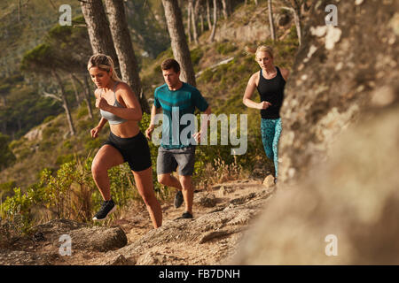 Group of runners running on rocks up a hill. Young people running cross country. Stock Photo