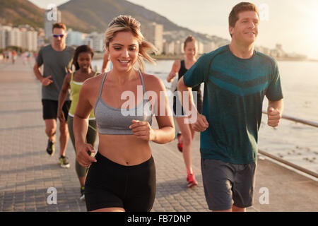 Portrait of fit young woman running with friends on street along the sea. Running club group training outdoors.