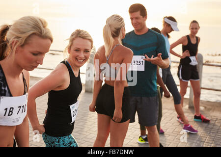 Group of happy young athletes standing on starting line and talking before start of the race. Running club group preparing for m Stock Photo