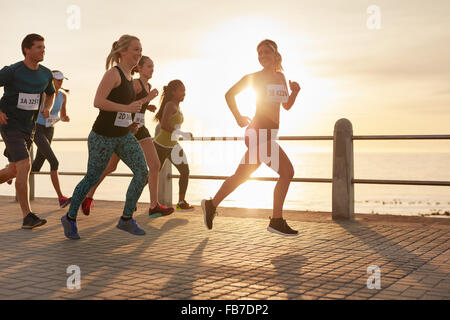 Fit young people running on street by the sea. Runners competing in a marathon race in evening. Stock Photo