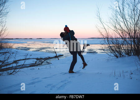 Full length of young man picking up woman and kissing on snow covered field Stock Photo
