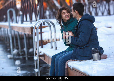 Happy young couple having coffee while sitting on pier Stock Photo