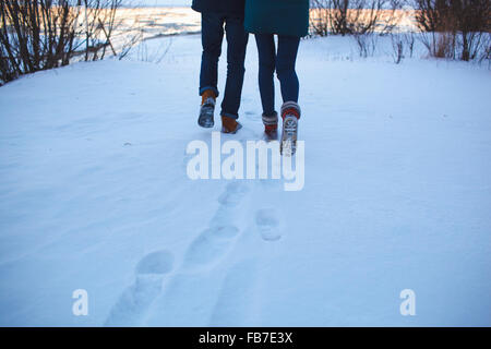 Low section of young couple walking on snowy field Stock Photo