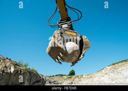 Low angle view of excavator claw picking sphere rock against clear blue sky Stock Photo