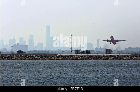 An aircraft takes off from JFK Airport against a backdrop of the hazy New York Skyline. Stock Photo