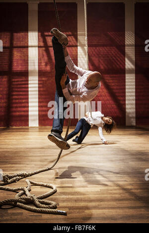 Man in mid-air pulling woman tied to rope against wall Stock Photo