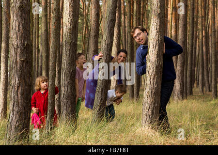 Happy family hiding behind tree trunks in forest Stock Photo