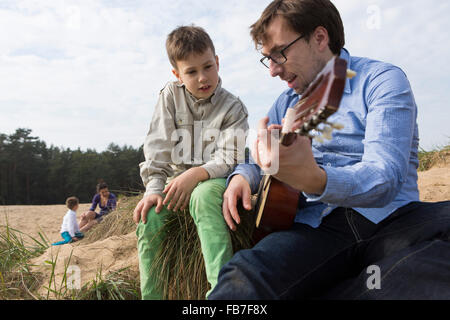 Boy looking at father playing guitar on field Stock Photo